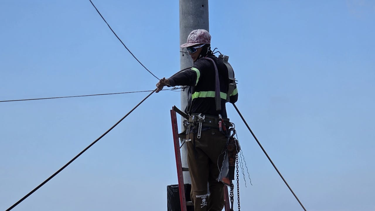 Electrical linemen working together at height on a power pole