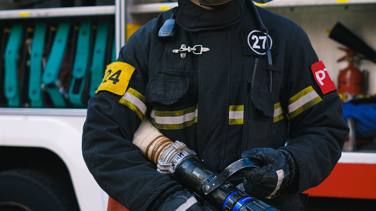 Firefighter with professional equipment and protective gear standing by fire truck