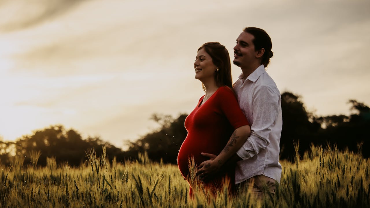 Couple outdoors for maternity portrait session, man hugging pregnant partner from behind