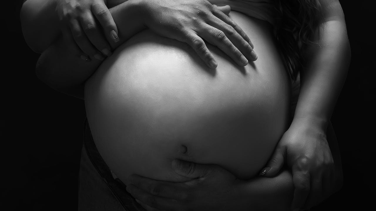 Black and white studio maternity portrait of couple with hands on pregnant belly