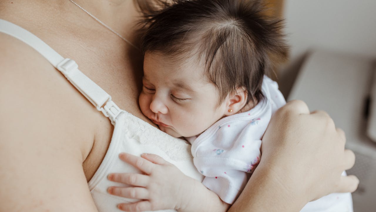 New mom wearing delicate gold necklace while holding newborn